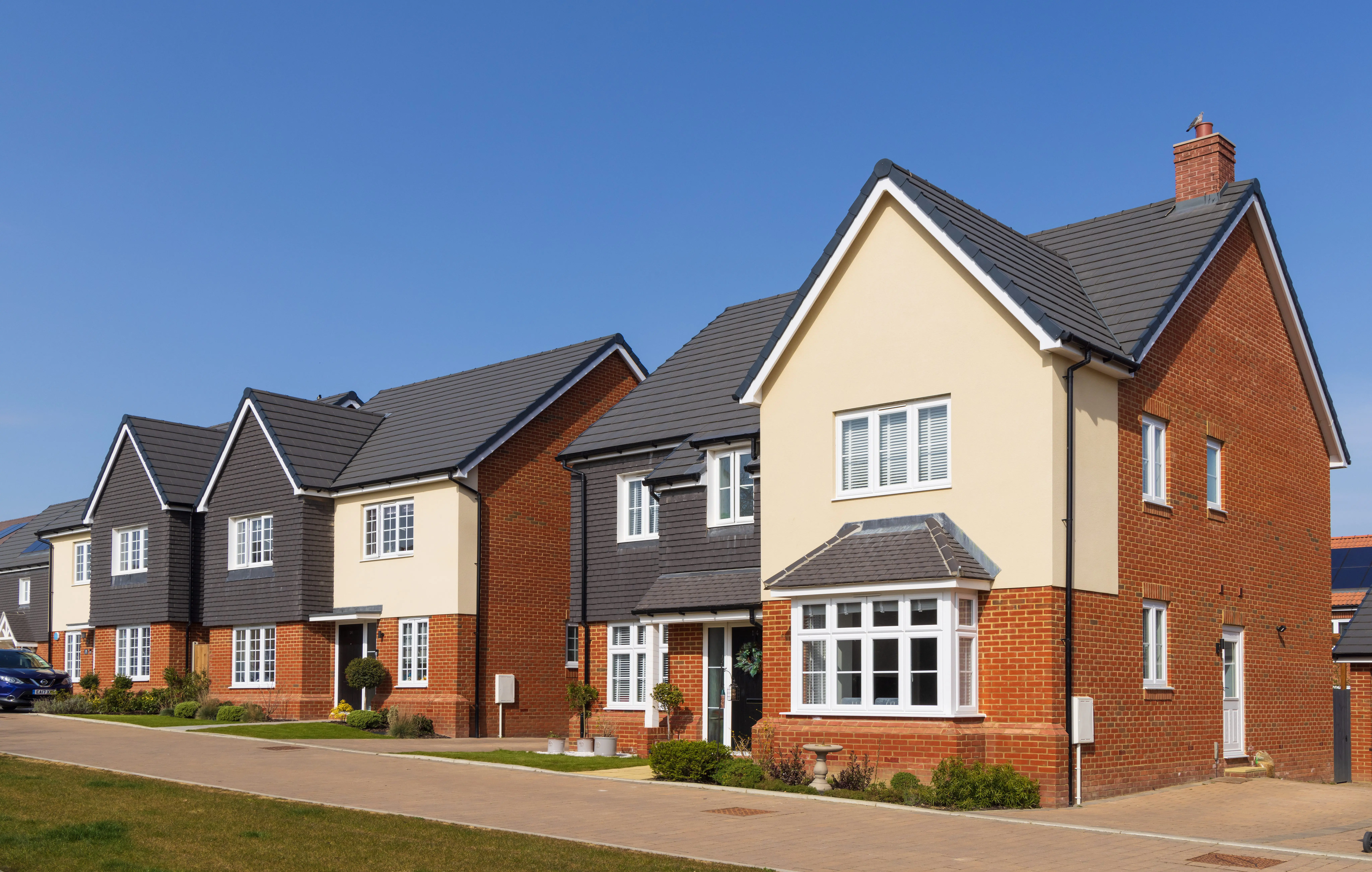 Row of modern detached houses with brick and cream exteriors on a sunny day.