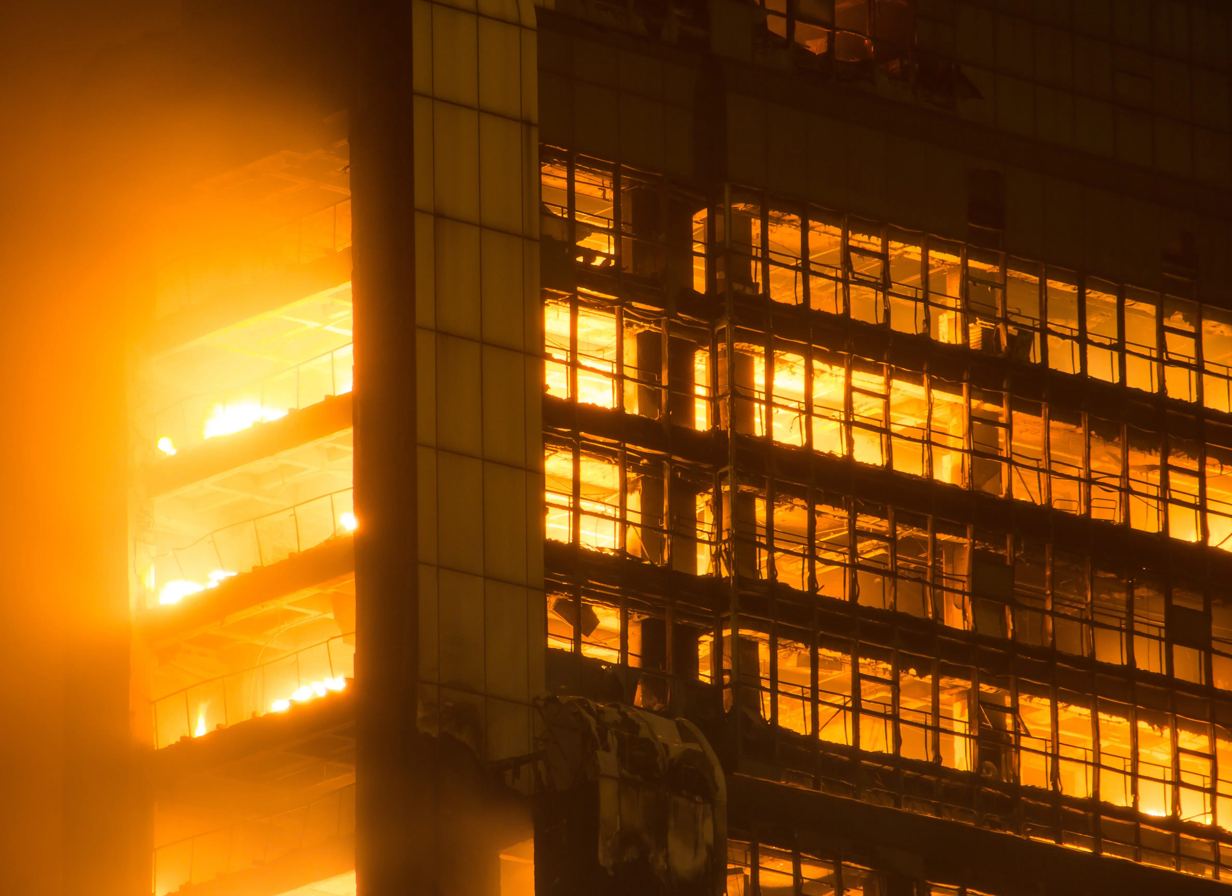 Fire engulfs multiple floors of a high-rise building at night, with intense orange flames visible inside.