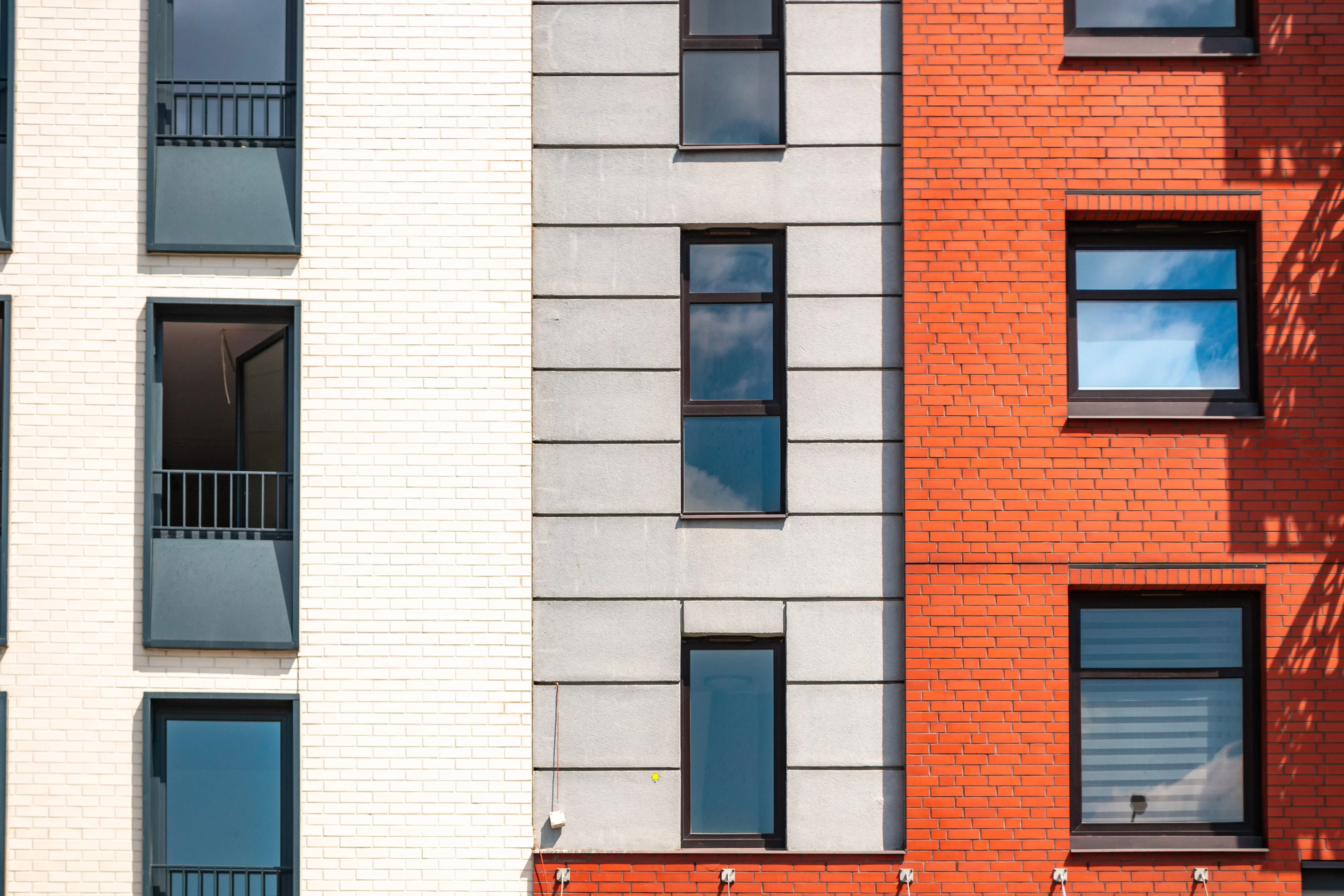Facade of a modern building with white, gray, and red brick sections and several windows.