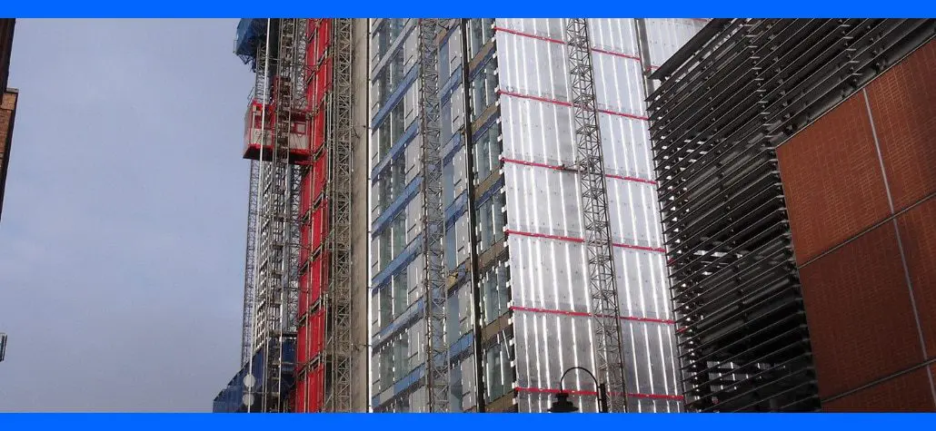 High-rise building under construction with scaffolding and metal paneling, viewed from street level.