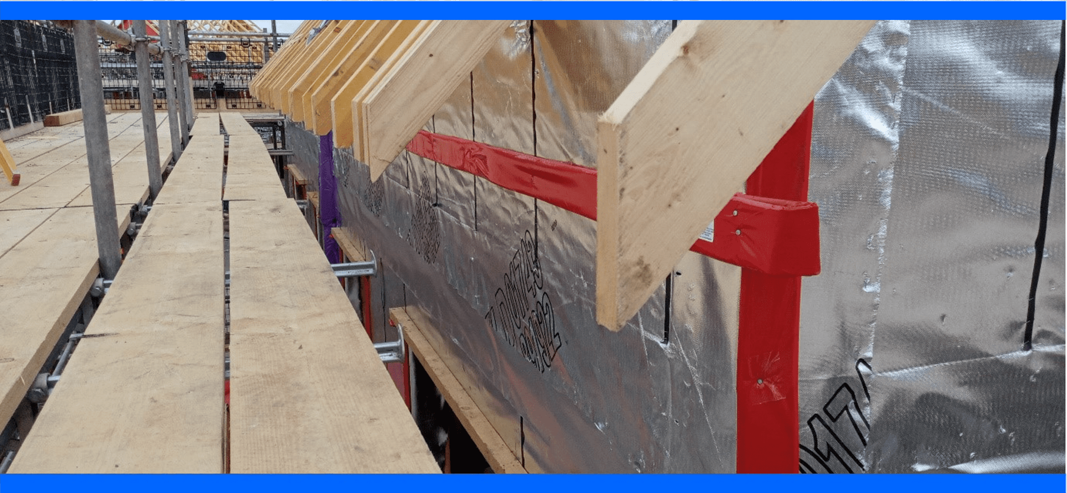 Wooden beams and foil insulation on a building under construction, viewed from a scaffolding walkway.