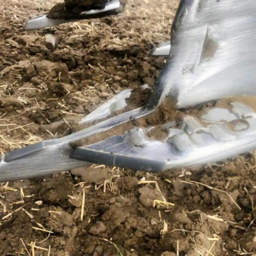 Close-up of a metal plow blade with soil stuck to it, cutting through dirt in a field.