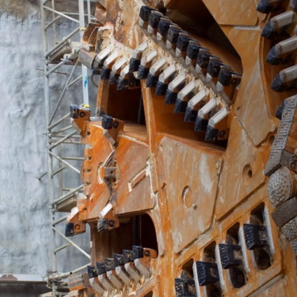 Close-up of an industrial tunnel boring machines rotating cutting head near a concrete wall and scaffolding.