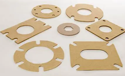 Seven variously shaped brown gaskets with holes are arranged on a light surface.