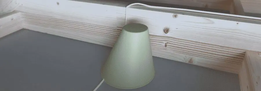 Green lamp placed on a gray surface next to a light wooden frame, with its cord trailing behind.