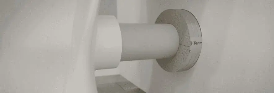 Close-up of a roll of toilet paper on a holder attached to a white bathroom wall.