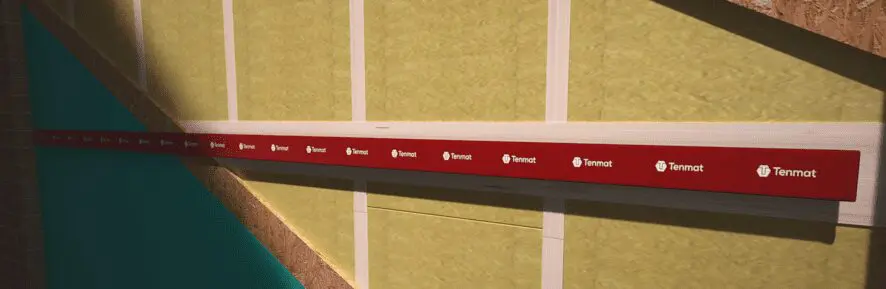 A red Termat level tool checks alignment on a green insulated wall under construction.