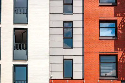 Close-up of a modern building facade with white, gray, and red brick sections and several windows.