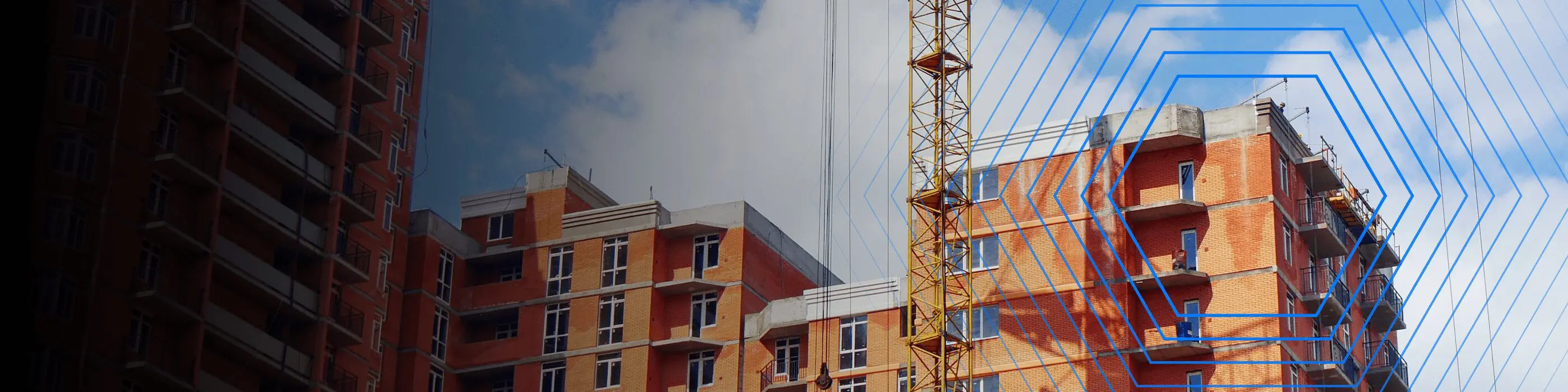 Red brick apartment buildings under construction with a yellow crane and blue sky in the background.