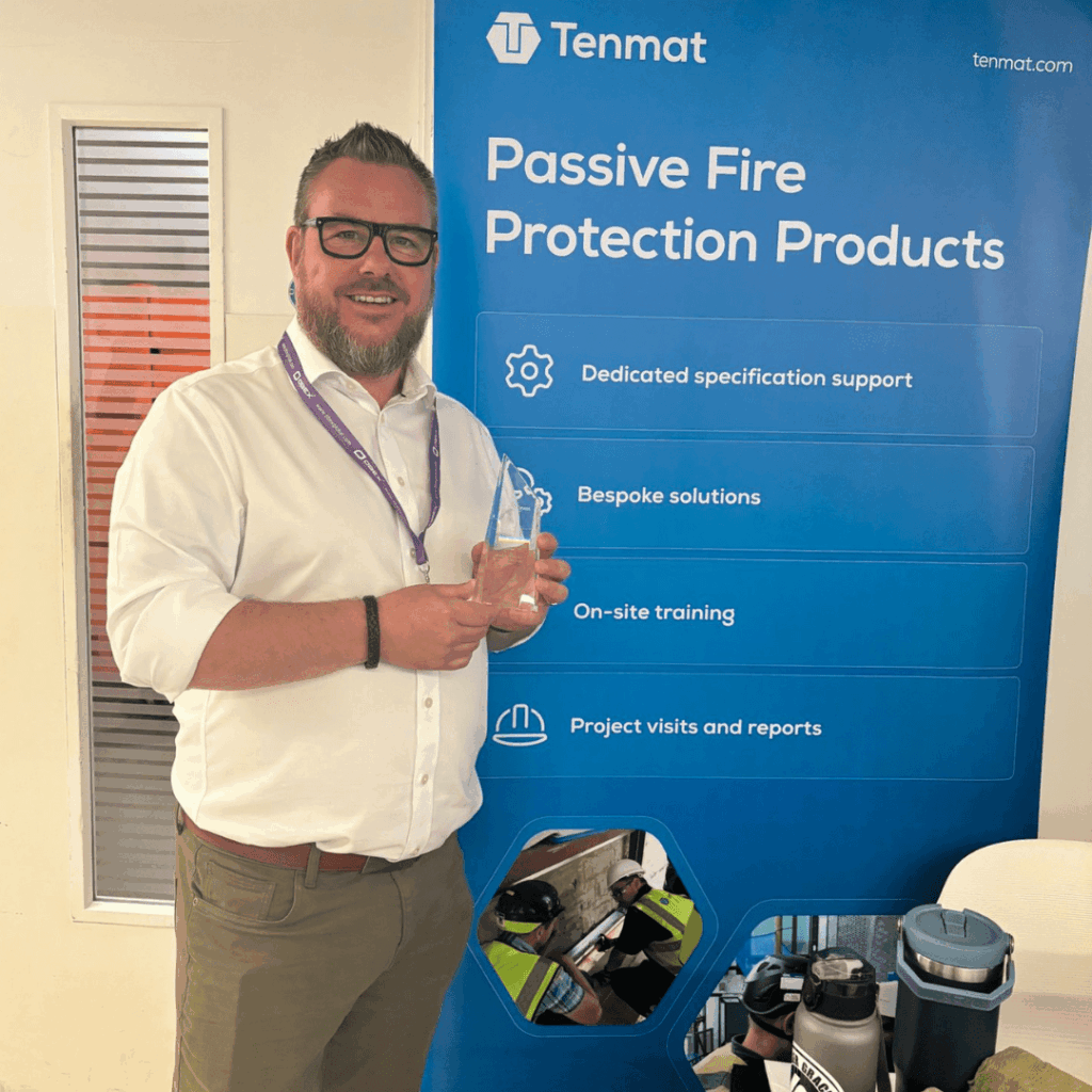 Man holding a glass award in front of a Tenmat Passive Fire Protection Products display banner.