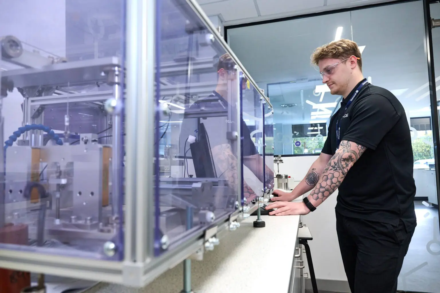 Tattooed person runs machinery in a sleek, modern lab or industrial workspace.