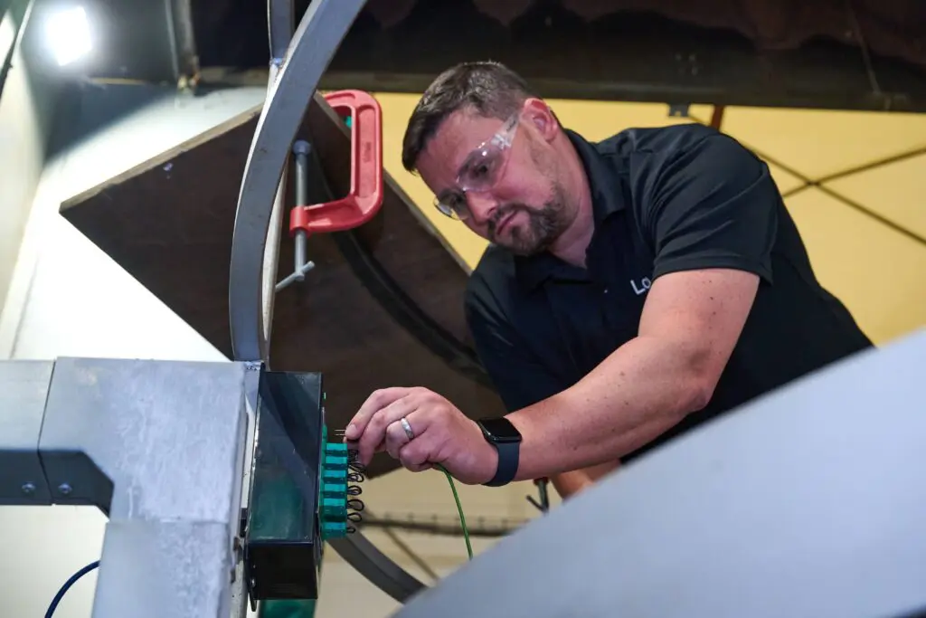 Man with safety glasses adjusts wires on industrial equipment.