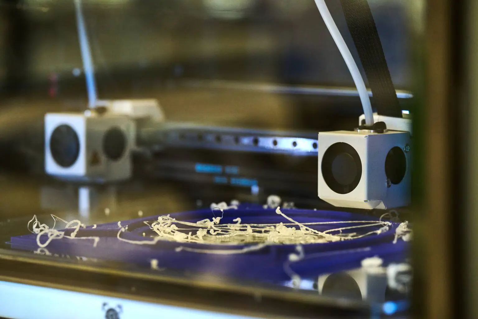3D printer close-up with white filament scattered across the print bed.