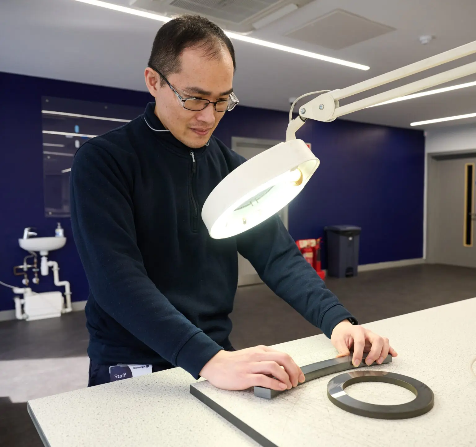 Man using tools under a bright lamp in a modern lab.