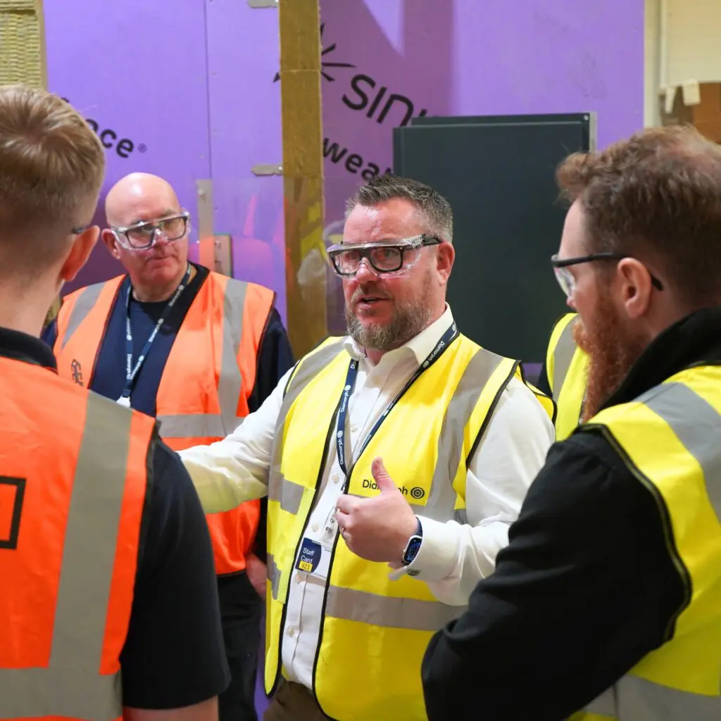 Men in safety vests talk about fire protection at a construction training site.