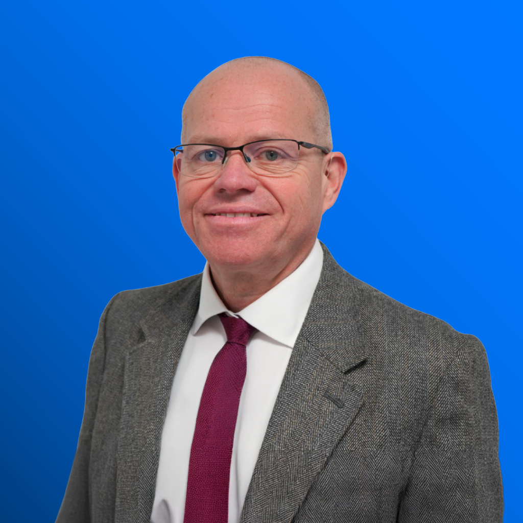 Man in suit, glasses, and red tie smiling before a blue background.