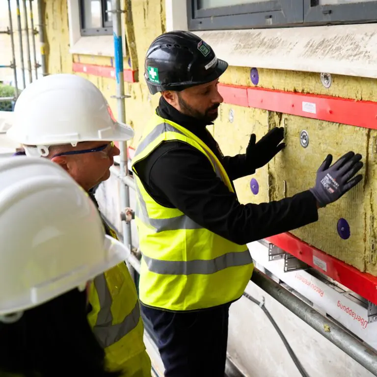 Two workers attach insulation panels to a building exterior.