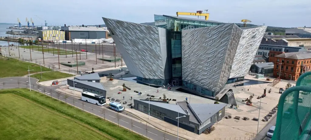 Modern, angular metallic building in a city, with grass patches and roads nearby.