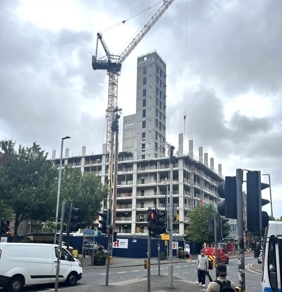 Skyscraper under construction with crane and city traffic at busy crossroads.