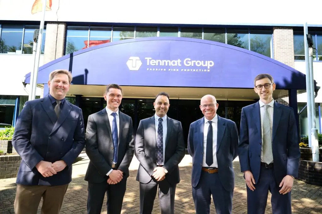 Five men in suits smile outside a Tenmat Group building with a blue canopy.