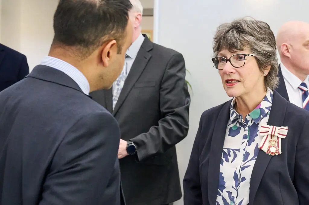 Woman with medal talks to suited man at indoor event, others around.
