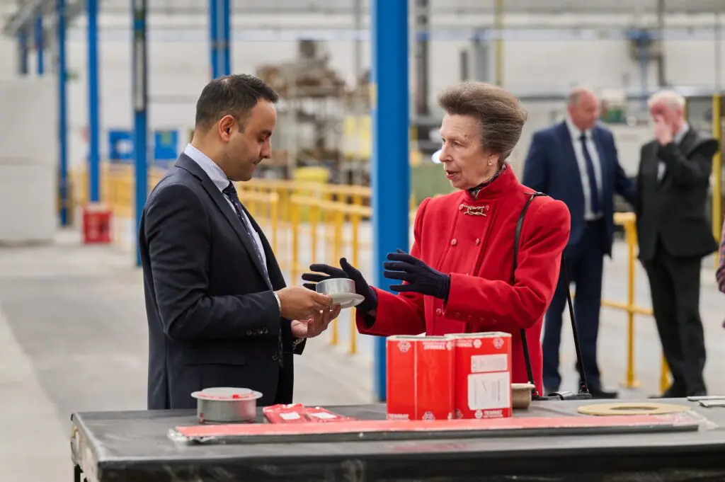 HRH talks to man holding object in an industrial warehouse.