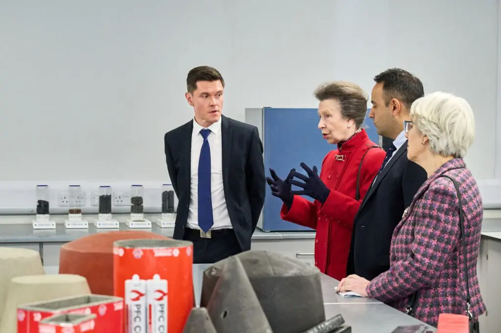 Four people in formalwear talk in a modern lab with visible equipment.