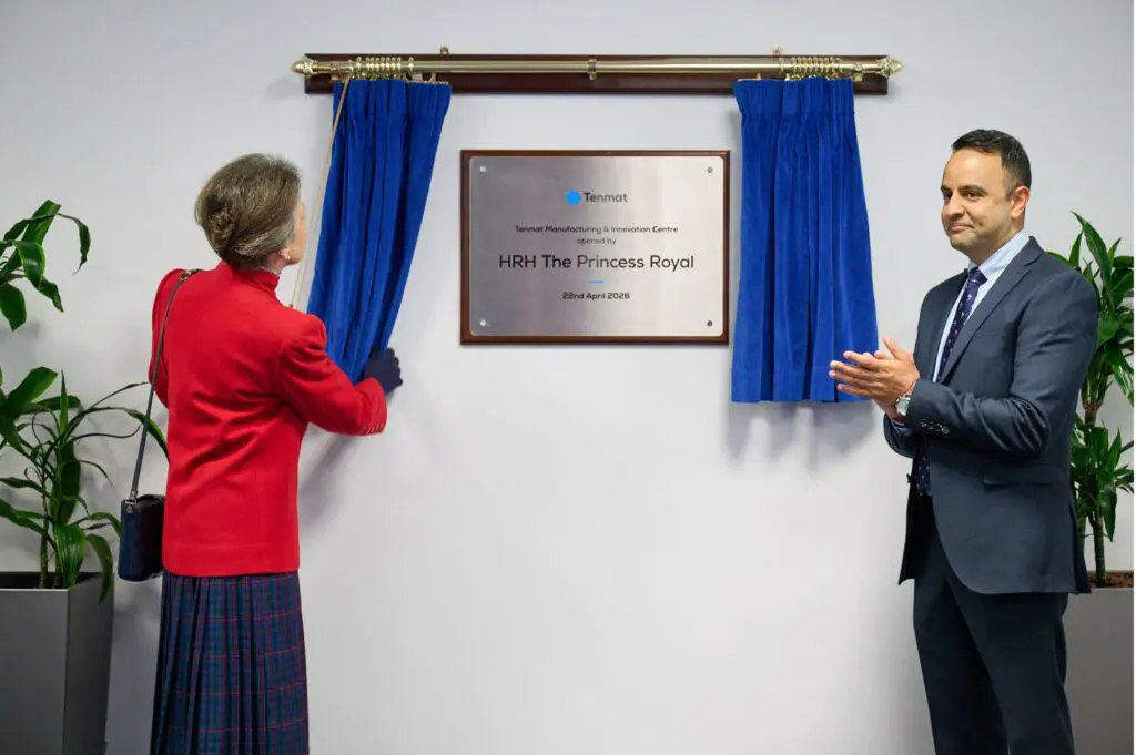 A woman unveils a plaque as a man applauds beside her in a formal setting.