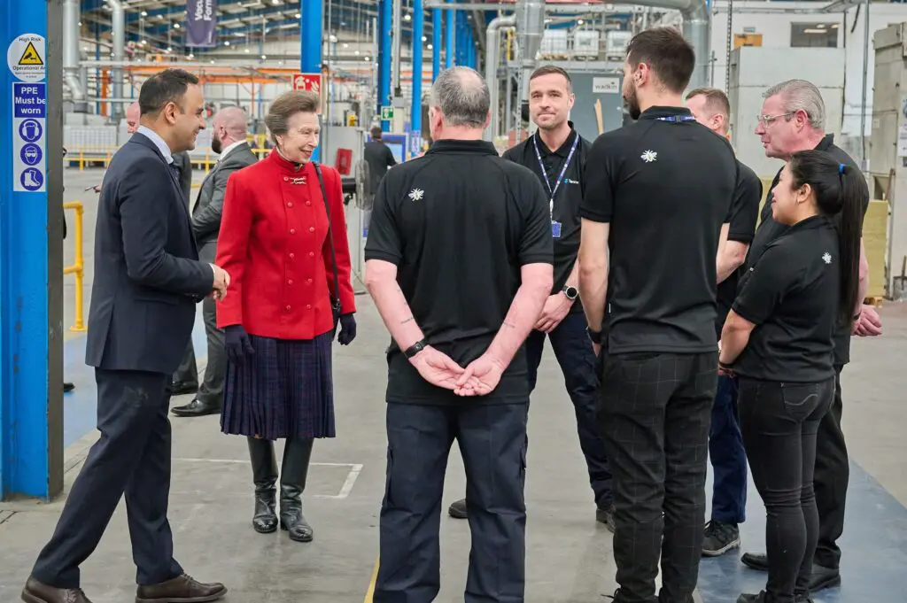 The Princess Royal talks to people in black uniforms inside a factory.