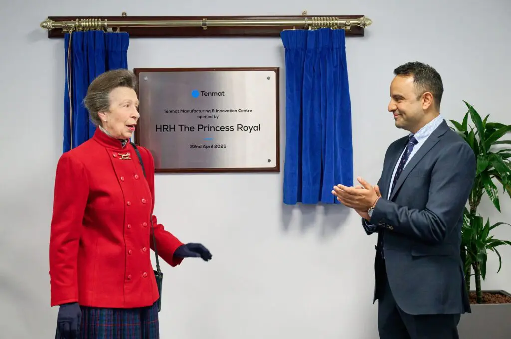 The Princess Royal speaks; man in suit applauds by a commemorative plaque on the wall.