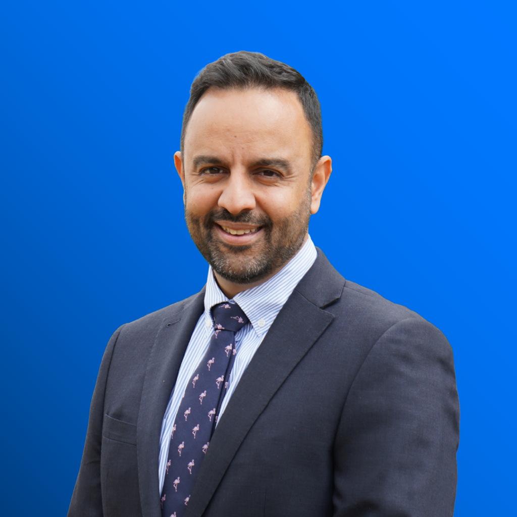 Man in suit and tie stands before a bright blue gradient background, smiling.