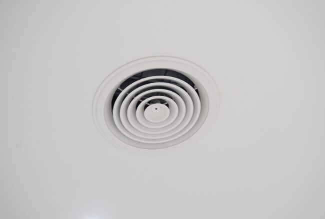 Extractor,Fan,On,The,Ceiling,Of,The,Office,Building A white circular air vent or ceiling diffuser on a plain white ceiling.