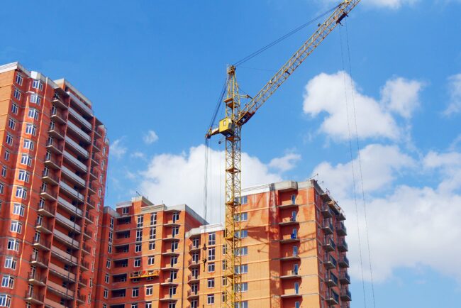 Construction,Site,Background.,High-rise,Red,Brick,Building,Under,Construction.,Crane Yellow construction crane beside unfinished red brick apartments under a blue sky with scattered clouds.