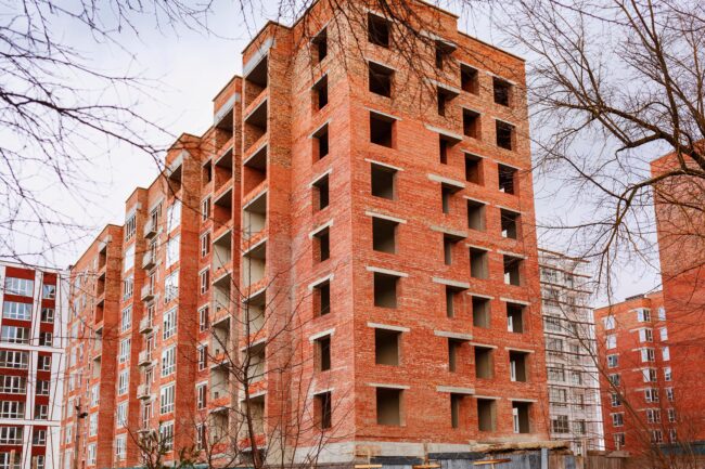 Construction,Site,Of,Brick,High-rise,Buildings.,Working,On,Building,Construction Unfinished brick apartment buildings with empty window openings and bare trees in front.