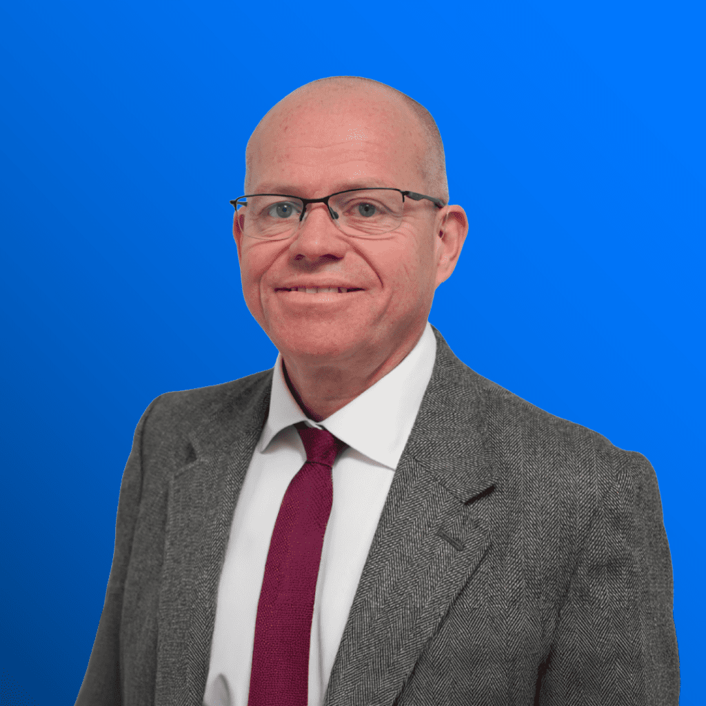 Man in suit, glasses, and red tie smiling before a blue background.