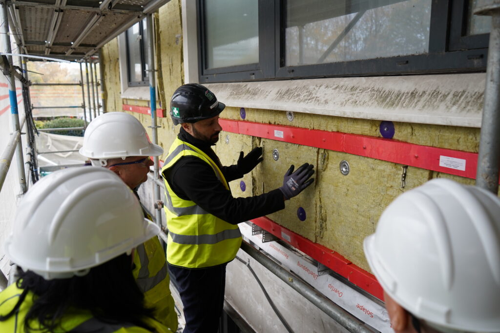 Workers in hard hats check insulation on a building under construction.