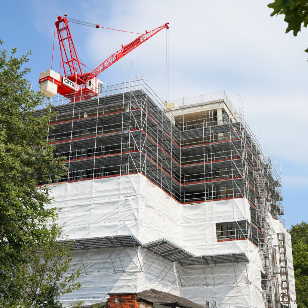 Building under construction with scaffolding; red crane stands tall against blue sky.