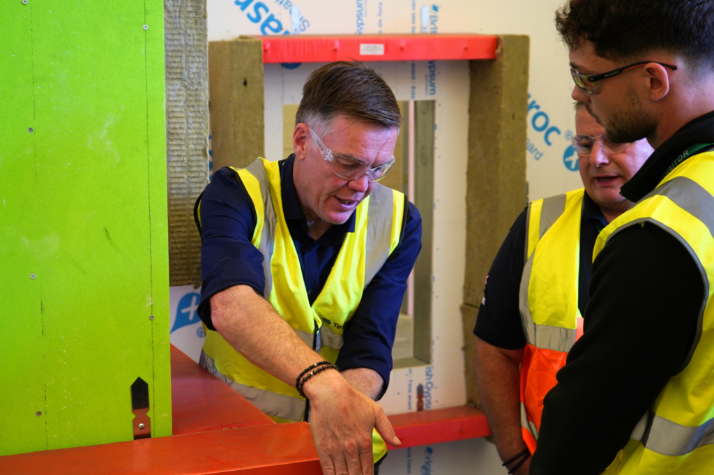 Man in safety vest discusses construction plans with two people at a building site.