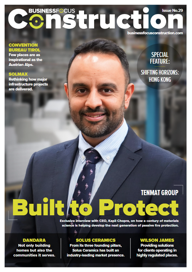 Smiling man in suit before blurred cityscape on a construction magazine cover.