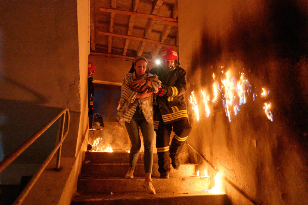 Firefighter helps woman with baby down burning stairs during a rescue.